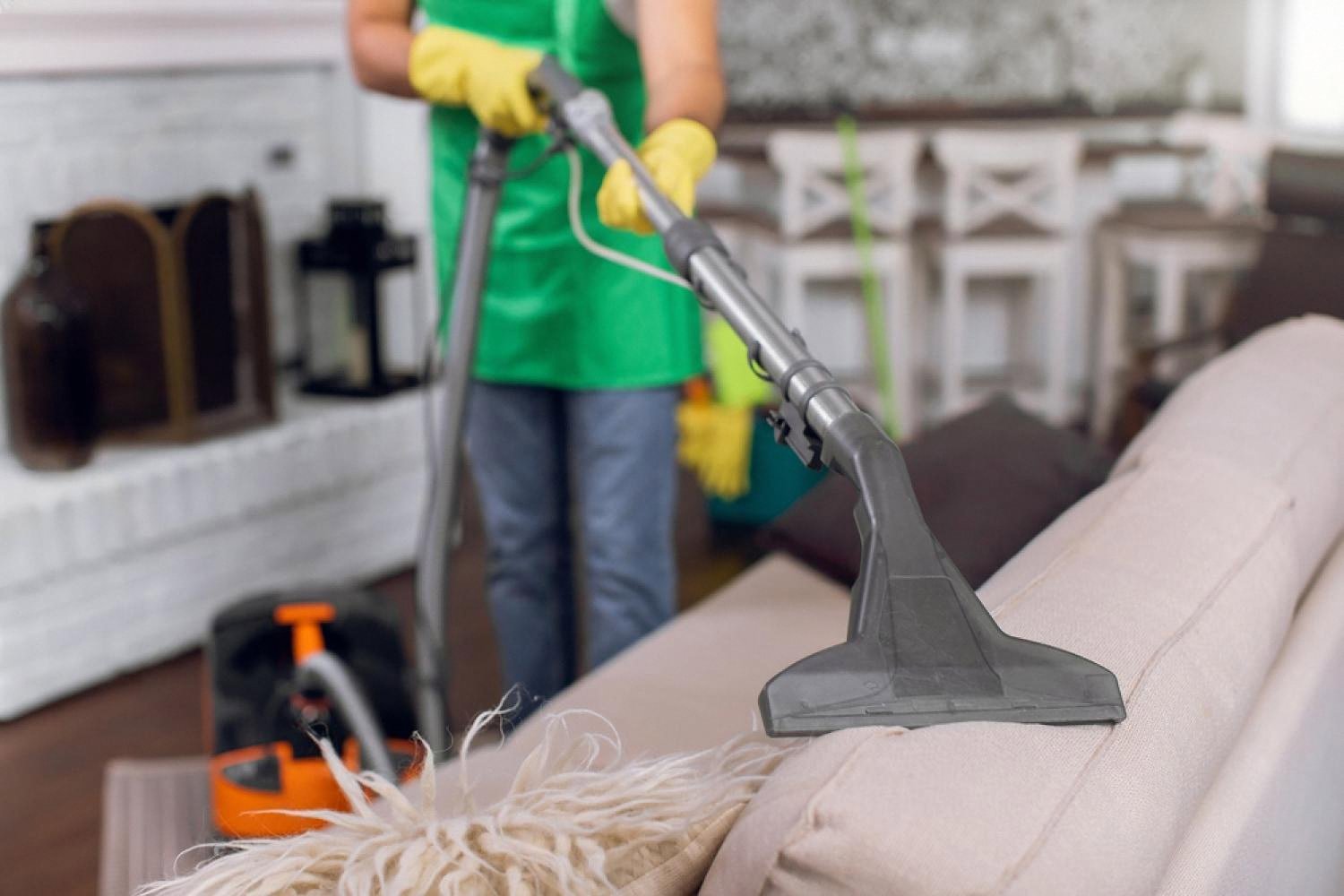 Professional using a hot water extraction wand on a beige sofa in Dubai